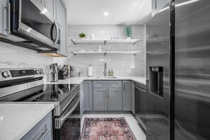 A modern kitchen with stainless steel appliances, marble countertops, and grey cabinetry. - Uhost AI 1BR With Marble Accents Patio (Fort Lauderdale)
