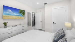 Un dormitorio moderno con una cama grande, una mesita de noche, un televisor en la pared y una puerta que da a un baño.