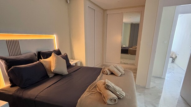 A modern hotel room with a large bed, a bedside table, and a mirror.