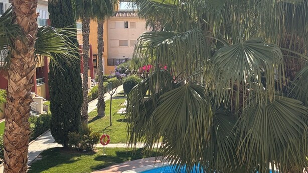 A swimming pool surrounded by palm trees and a building with a tiled roof. - Bel Appartement Moderne, six Personnes (Fuente Alamo)