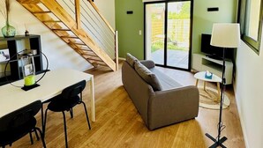 A modern living space with a wooden staircase, a dining area with a table and chairs, a sofa, a TV, and a lamp. - Le Petit *** - 1 room, all new & all inclusive (Montauban)