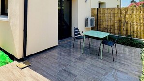 A modern building with a flat roof, a covered patio area with a table and chairs, and a wooden fence in the background. - Le Petit *** - 1 room, all new & all inclusive (Montauban)