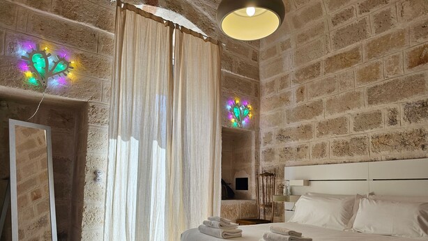 A bedroom with a large bed, a mirror, a window with curtains, and a brick wall. - Casetta Via Roma in Monopoli (Monopoli)