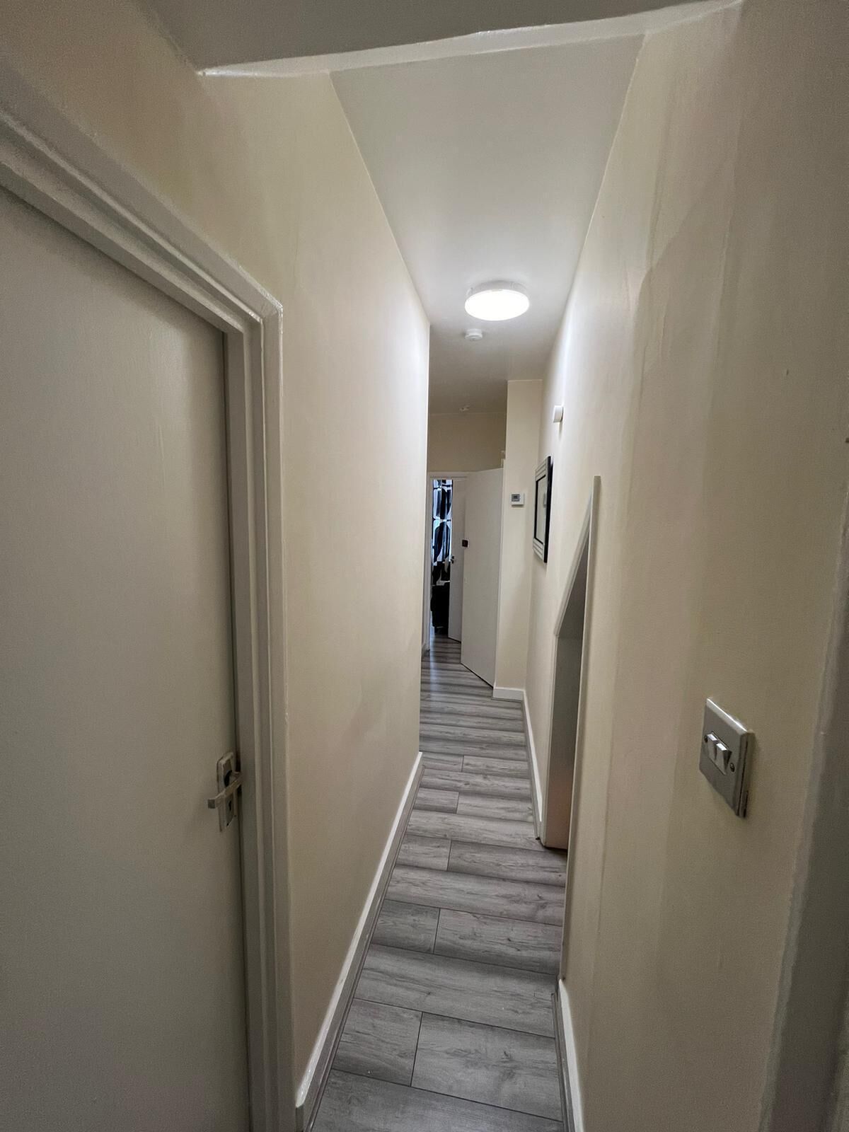 A narrow hallway with beige walls and a wooden floor.