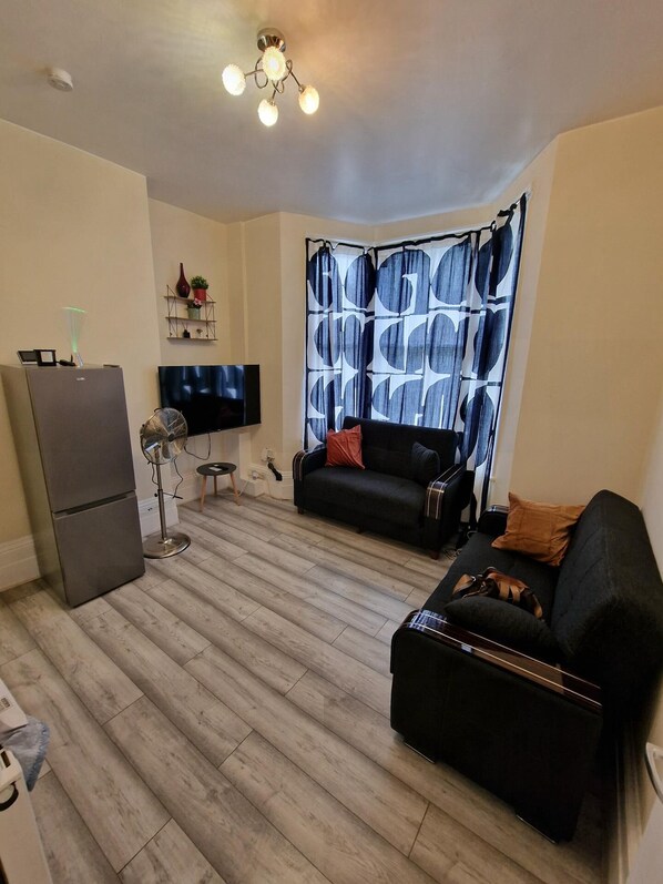 Una sala de estar con un sofá, un televisor, un refrigerador y una cortina estampada.