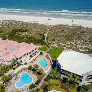 An aerial view of a resort with a large pool, a beach, and a building with a red roof.