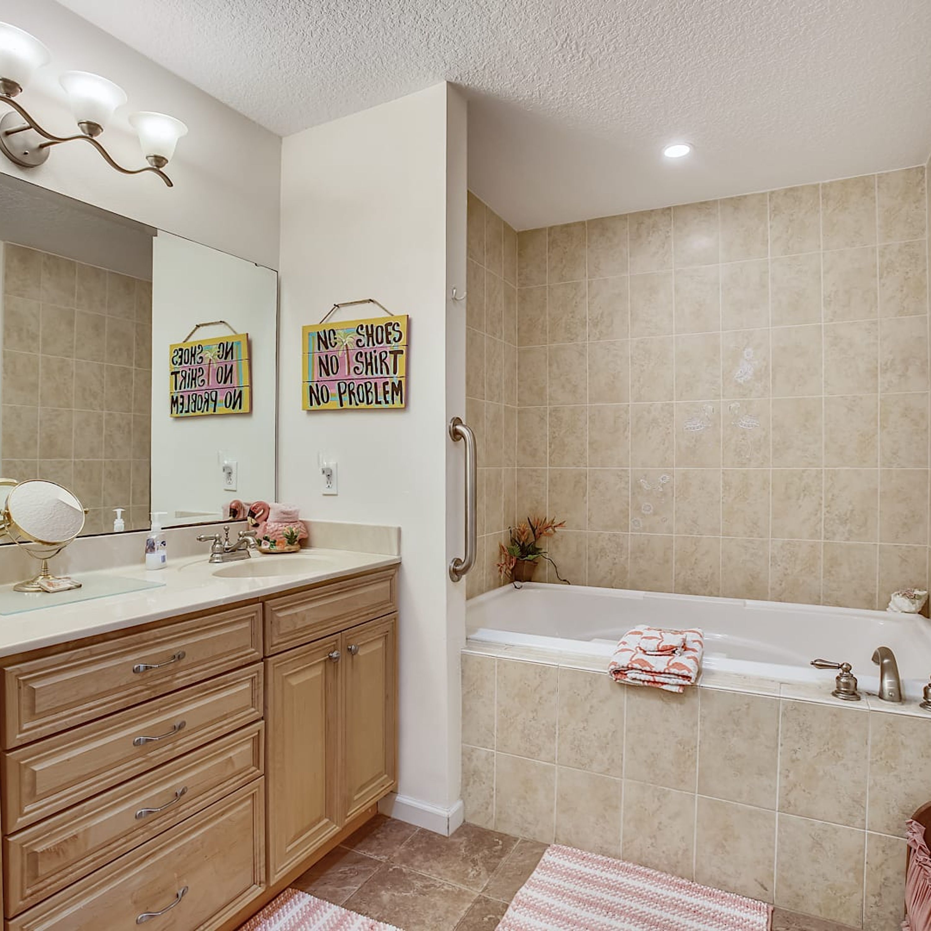 A bathroom with a sink, mirror, vanity, and a bathtub. There are two signs on the wall, one saying "NO SHOES NO SHIRT NO PROBLEM" and the other "NO SHOES NO SHIRT NO PROBLEM".