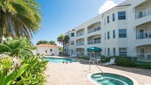 A pool area with lounge chairs and a hot tub, surrounded by a multi-story building with balconies. - Ocean Bliss 2BD Villa on St Augustine Beach (St. Augustine)