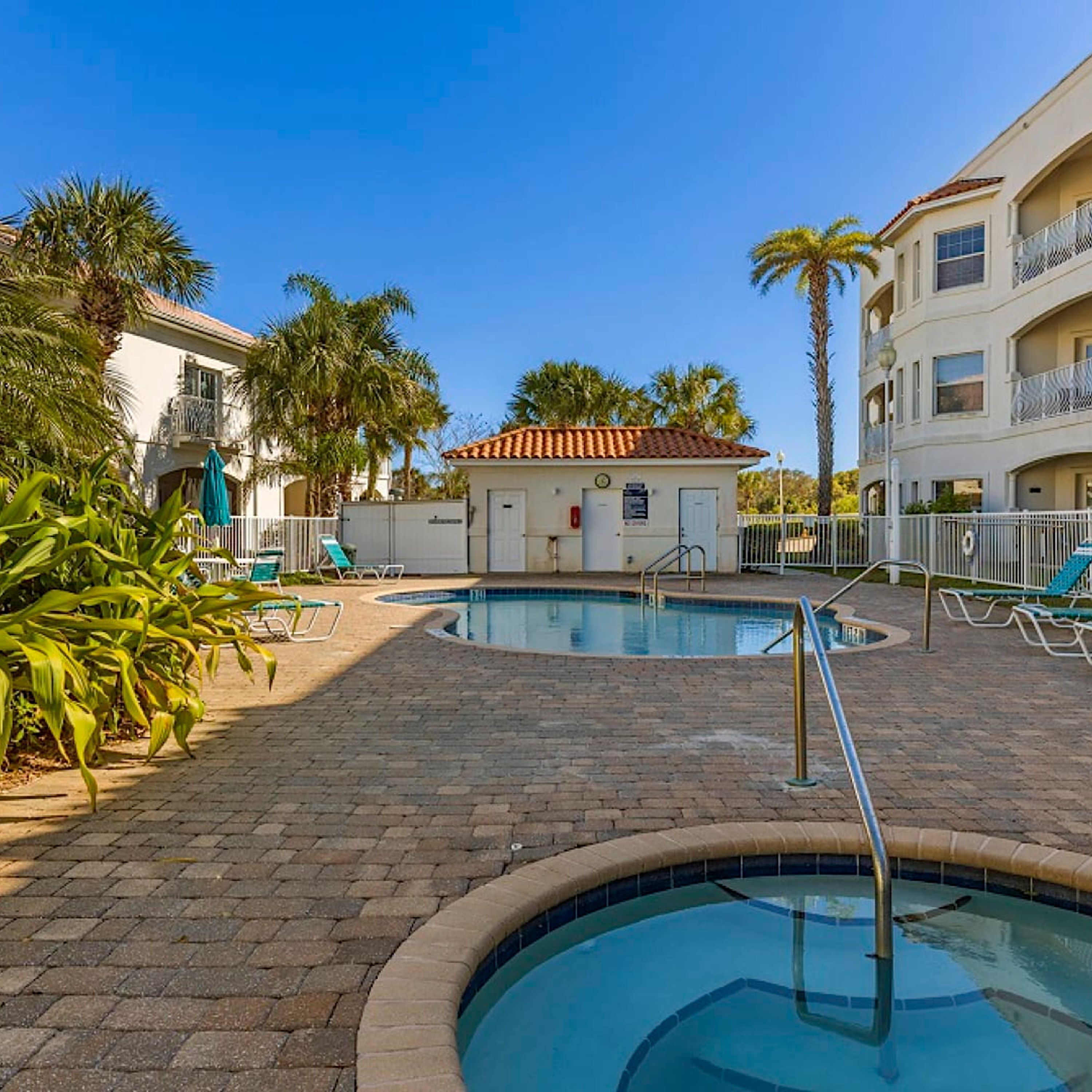 A pool area with two pools, palm trees, and a small building with a clock.