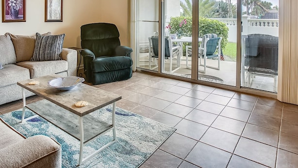A living room with a ceiling fan, a sofa, a chair, a coffee table, and a sliding glass door leading to an outdoor patio. - Ocean Bliss 2BD Villa on St Augustine Beach (St. Augustine)