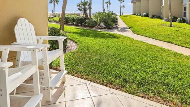 A covered outdoor area with a white Adirondack chair, a well-maintained lawn, and a row of palm trees. - Ocean Oasis Relax Near Historic St Augustine (St. Augustine)