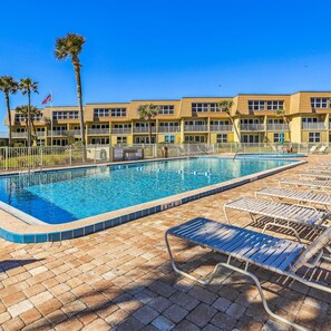 A swimming pool with lounge chairs, a fenced area, and a multi-story building with balconies. - Ocean Oasis Relax Near Historic St Augustine (St. Augustine)