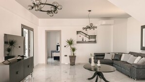 A modern living room with a large TV, a sofa, a coffee table, and a chandelier. - The Ionian Sea and Sunset View Villa (Minia)
