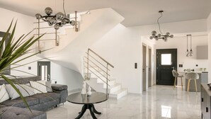 A modern living room with a grey sofa, a round black table, and a staircase with a chandelier. - The Ionian Sea and Sunset View Villa (Minia)