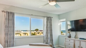 Une chambre dotée d’un grand lit, d’un ventilateur de plafond, d’une télévision et offrant une vue sur l’océan.