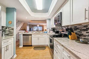 Una cucina moderna con mobili bianchi, un forno a microonde in acciaio inossidabile e uno schienale piastrellato.