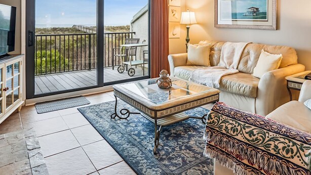 A living room with a balcony, a sofa, a coffee table, and a TV. - Oceanfront 3BR Luxe New Rental (St. Augustine)