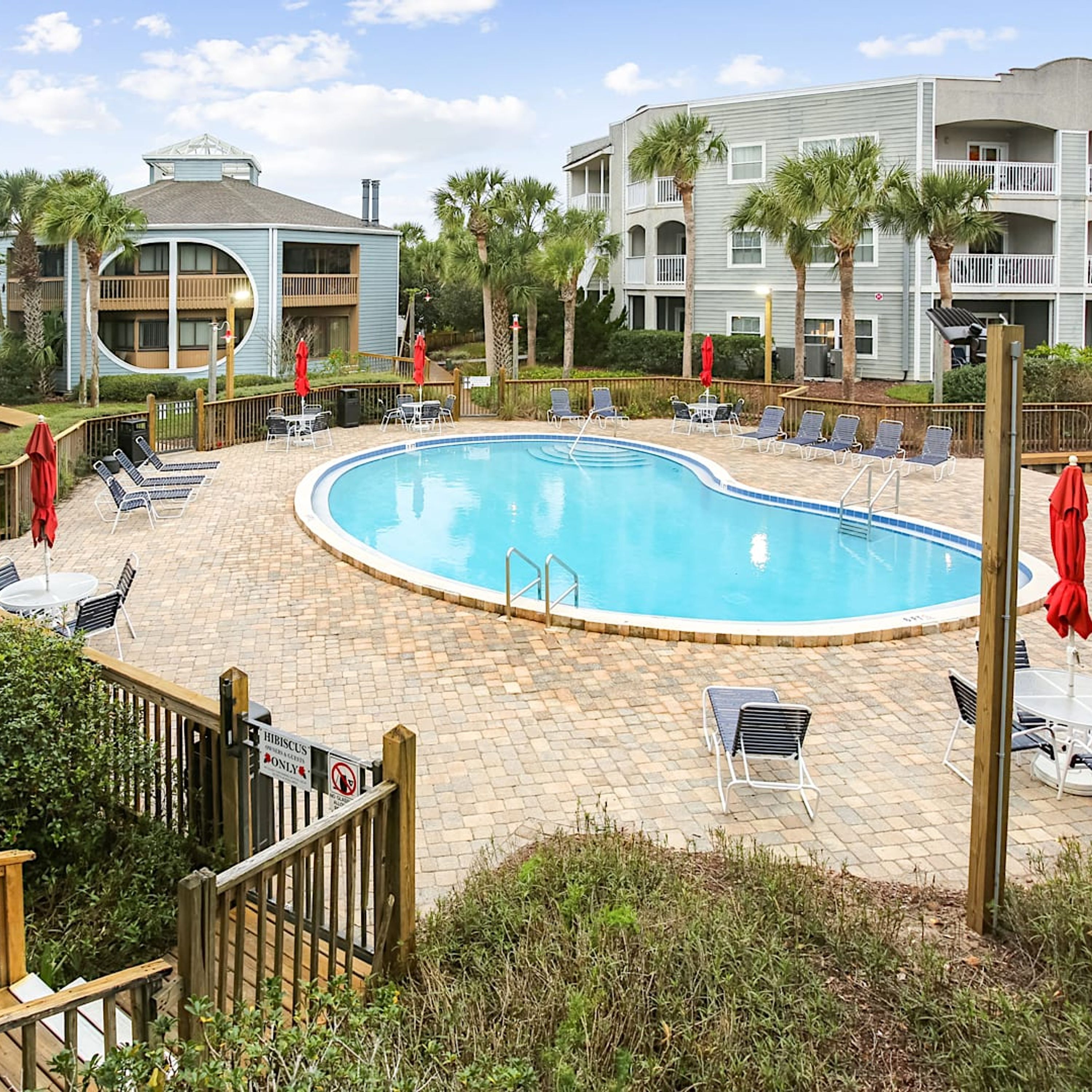 A pool area with lounge chairs and umbrellas, surrounded by a wooden deck and a fence.