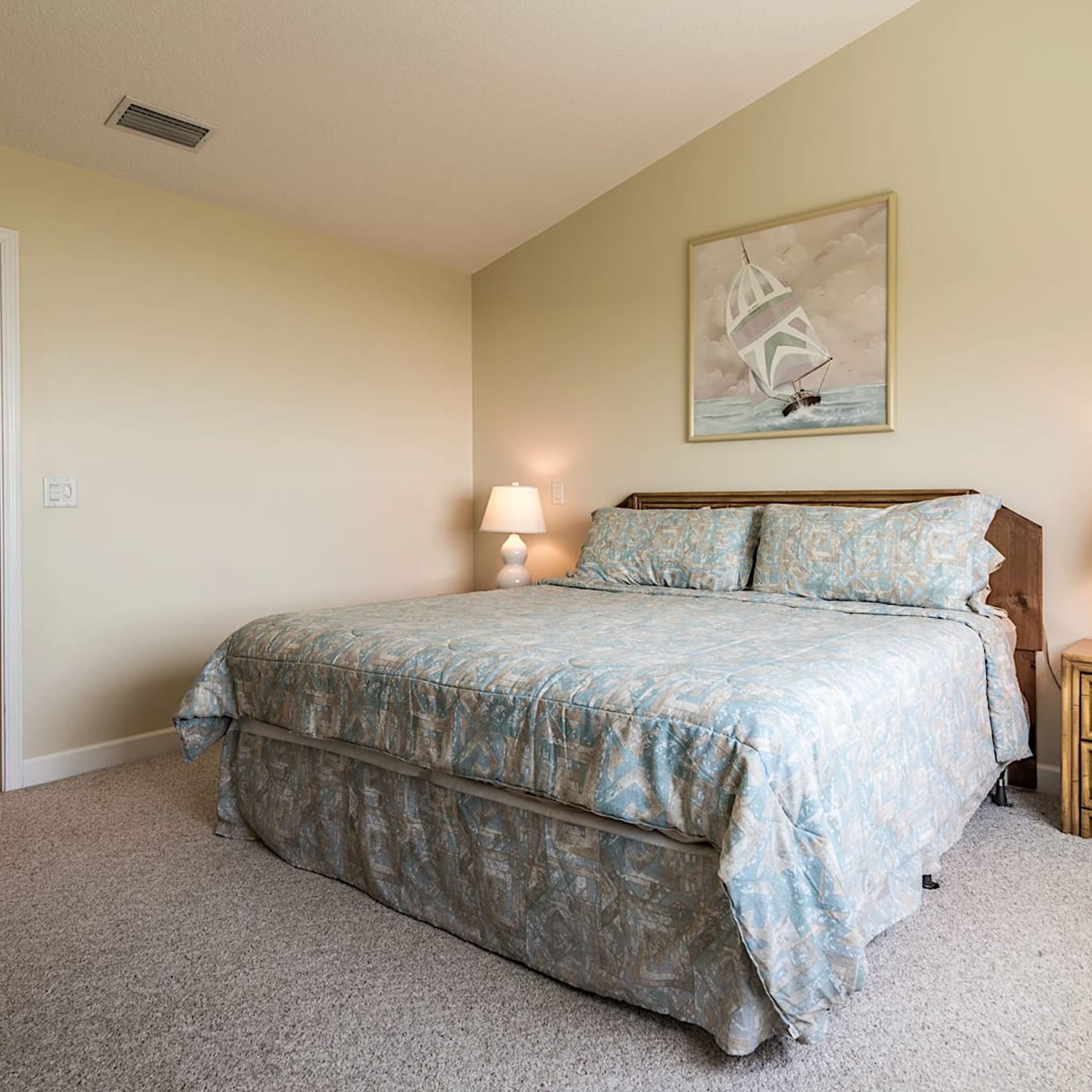 A bedroom with a bed, a nightstand, a lamp, and a painting on the wall.