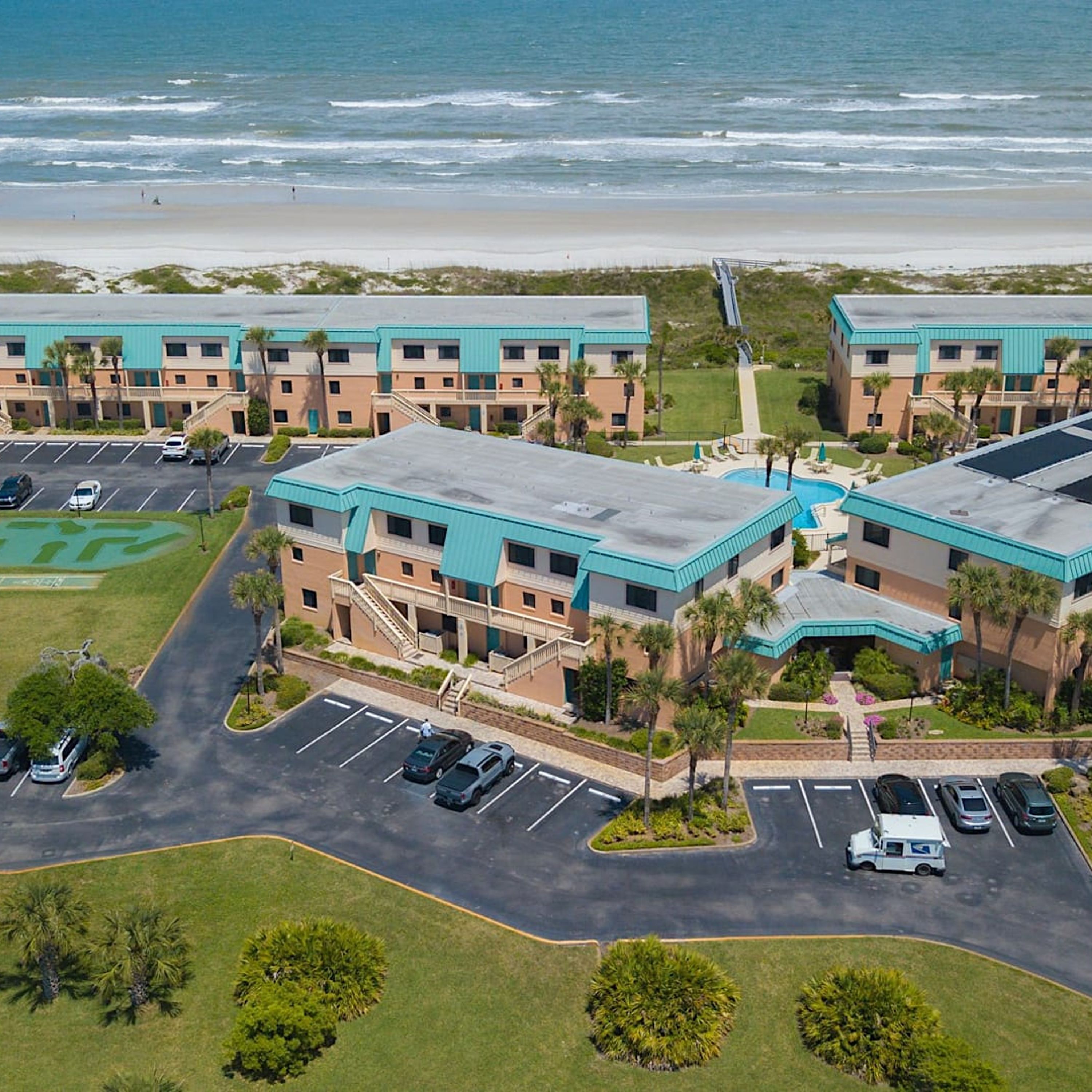 A beachfront hotel with multiple-story buildings, parking lots, and a pool area.