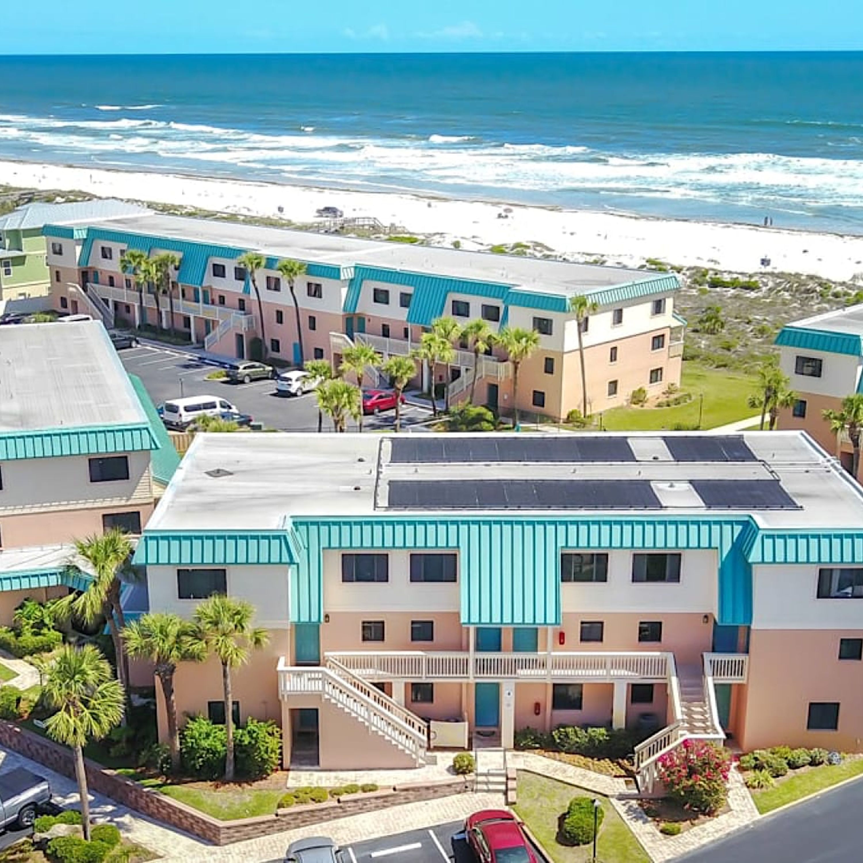 A beachfront hotel with multiple-story buildings, a parking lot, and a view of the ocean.