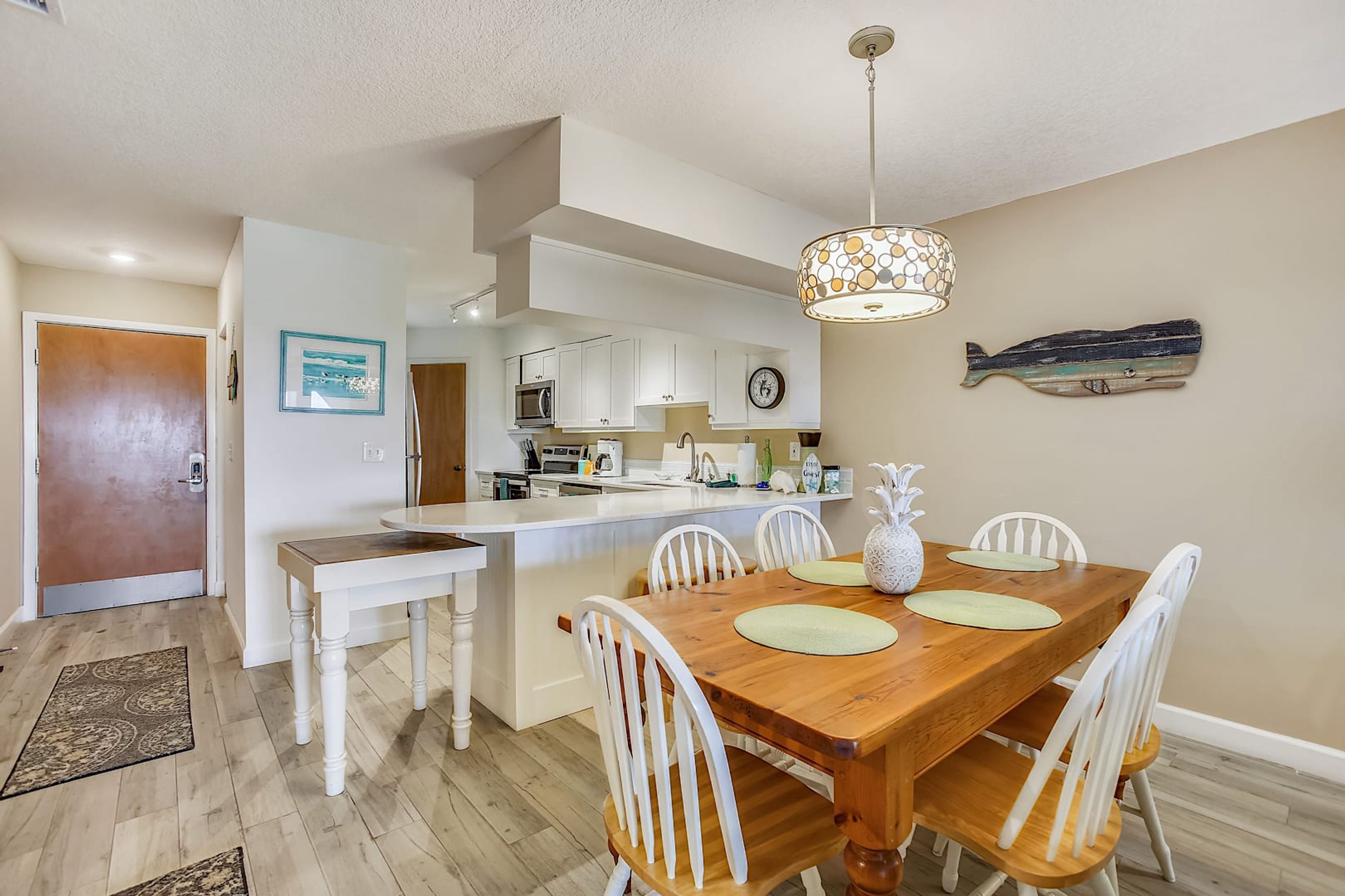 A modern kitchen with white cabinets, a wooden dining table with white chairs, and a pendant light.