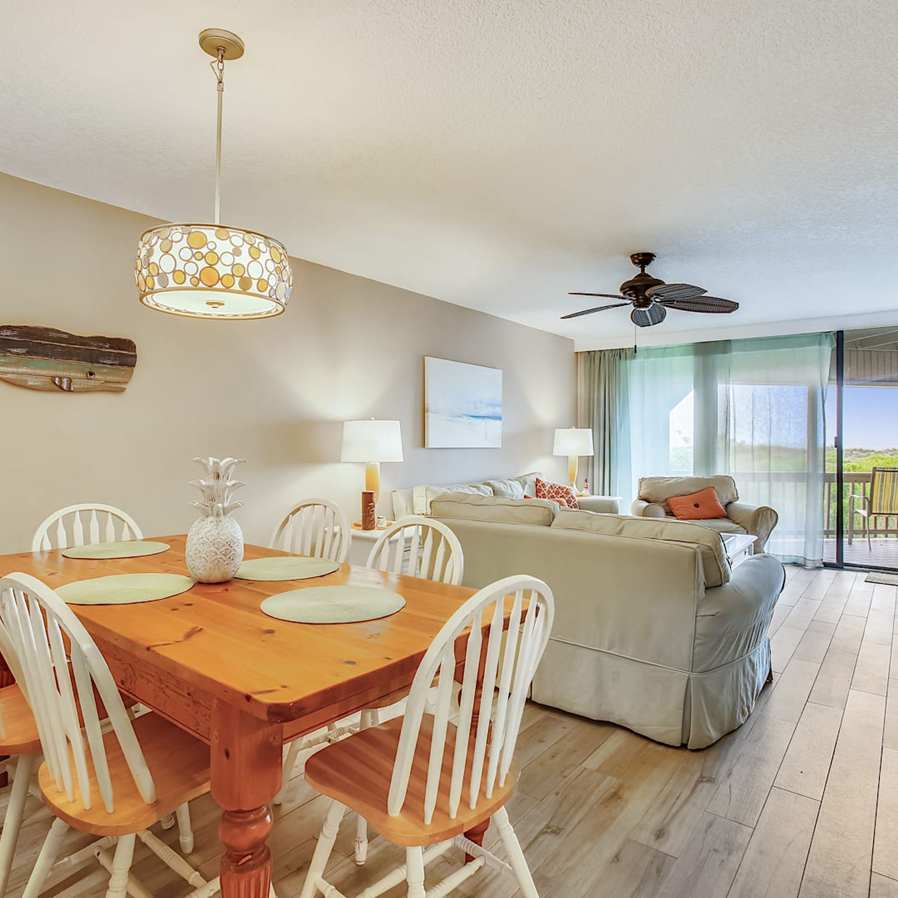 A spacious living area with a wooden dining table, white chairs, a sofa, and a ceiling fan.