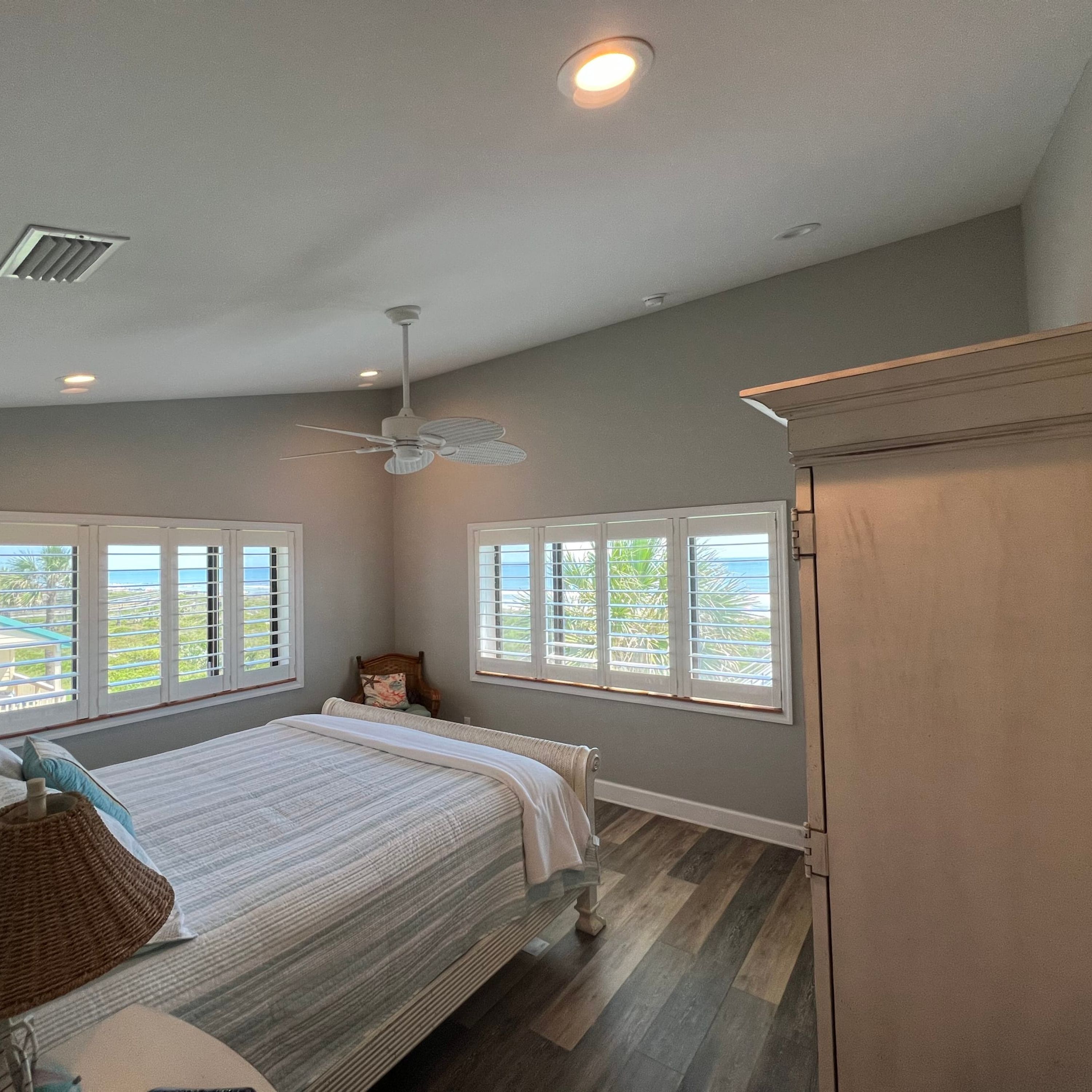 A bedroom with a bed, a chair, a ceiling fan, and windows with blinds.