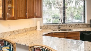 A kitchen with wooden cabinets, a granite countertop, and a window with blinds. - Oceanfront Oasis Hibiscus C202 St Aug Free Tix (St. Augustine)