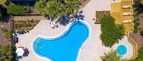 An aerial view of a swimming pool area with lounge chairs, a small pool, and surrounding greenery.
