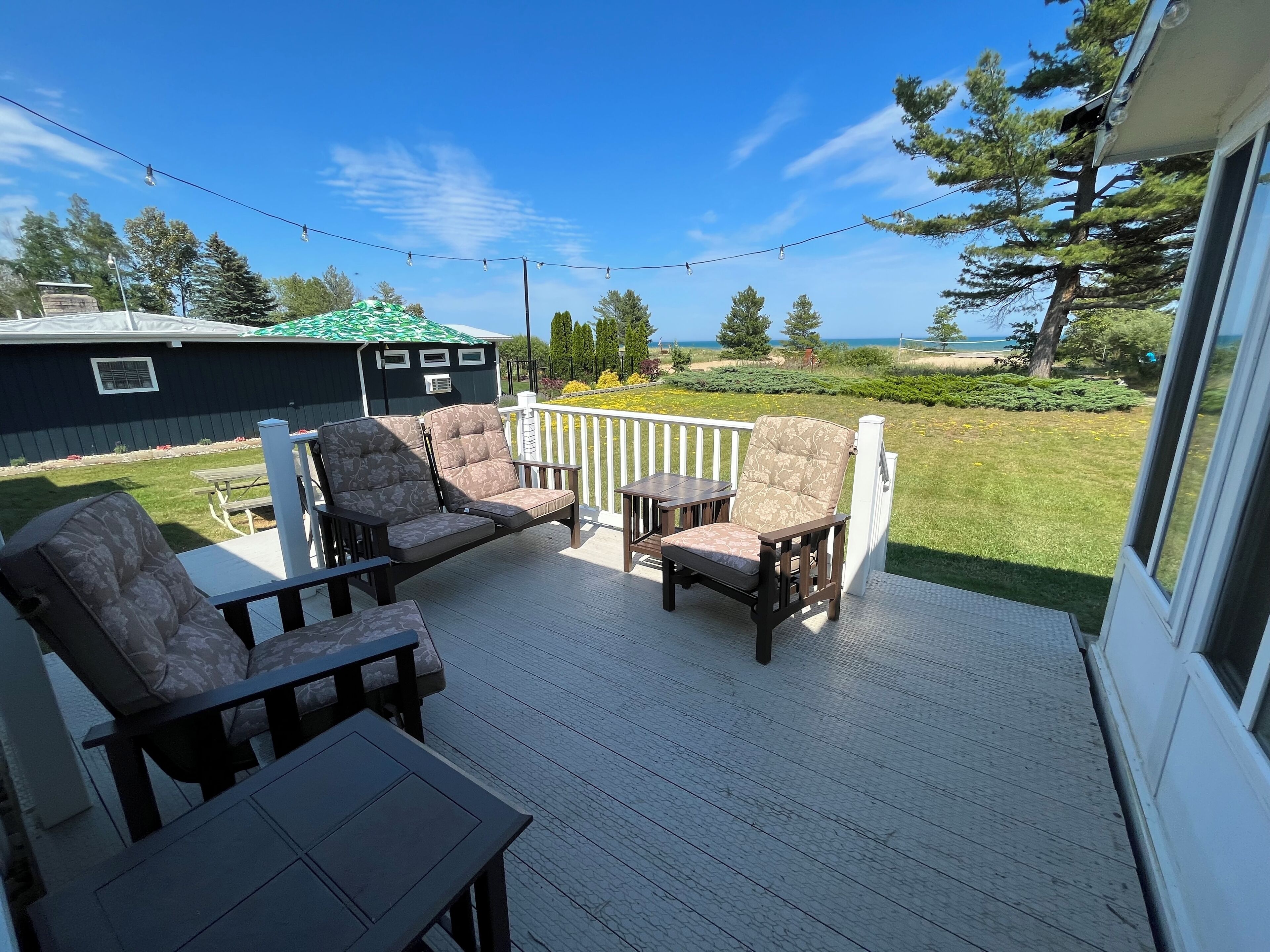 A deck with outdoor furniture, a view of the ocean, and a house in the background.