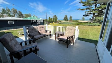 A deck with outdoor furniture, a view of the ocean, and a house in the background.