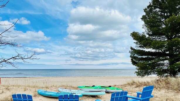 Une terrasse en bois avec quatre chaises Adirondack bleues, donnant sur une plage où l’on peut faire du kayak, et offrant une vue sur l’océan.