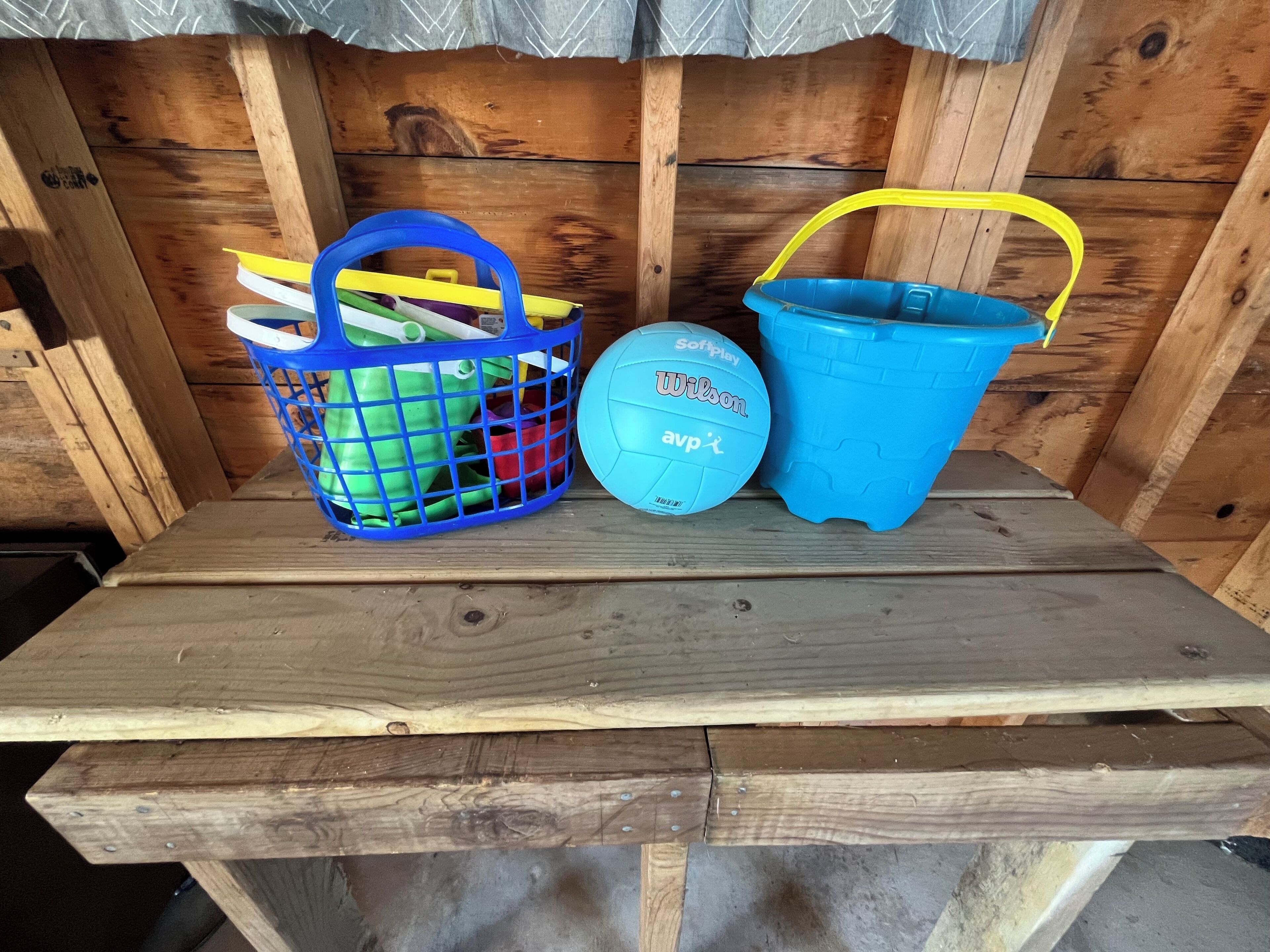 A wooden bench with a blue plastic basket and a blue plastic bucket.