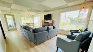 Un salon moderne avec un canapé gris, un fauteuil gris et un téléviseur fixé au mur au-dessus d’une cheminée en briques.