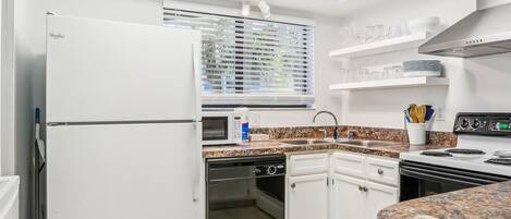 A compact kitchen with white cabinetry, a built-in oven, a microwave, and a stainless steel sink.