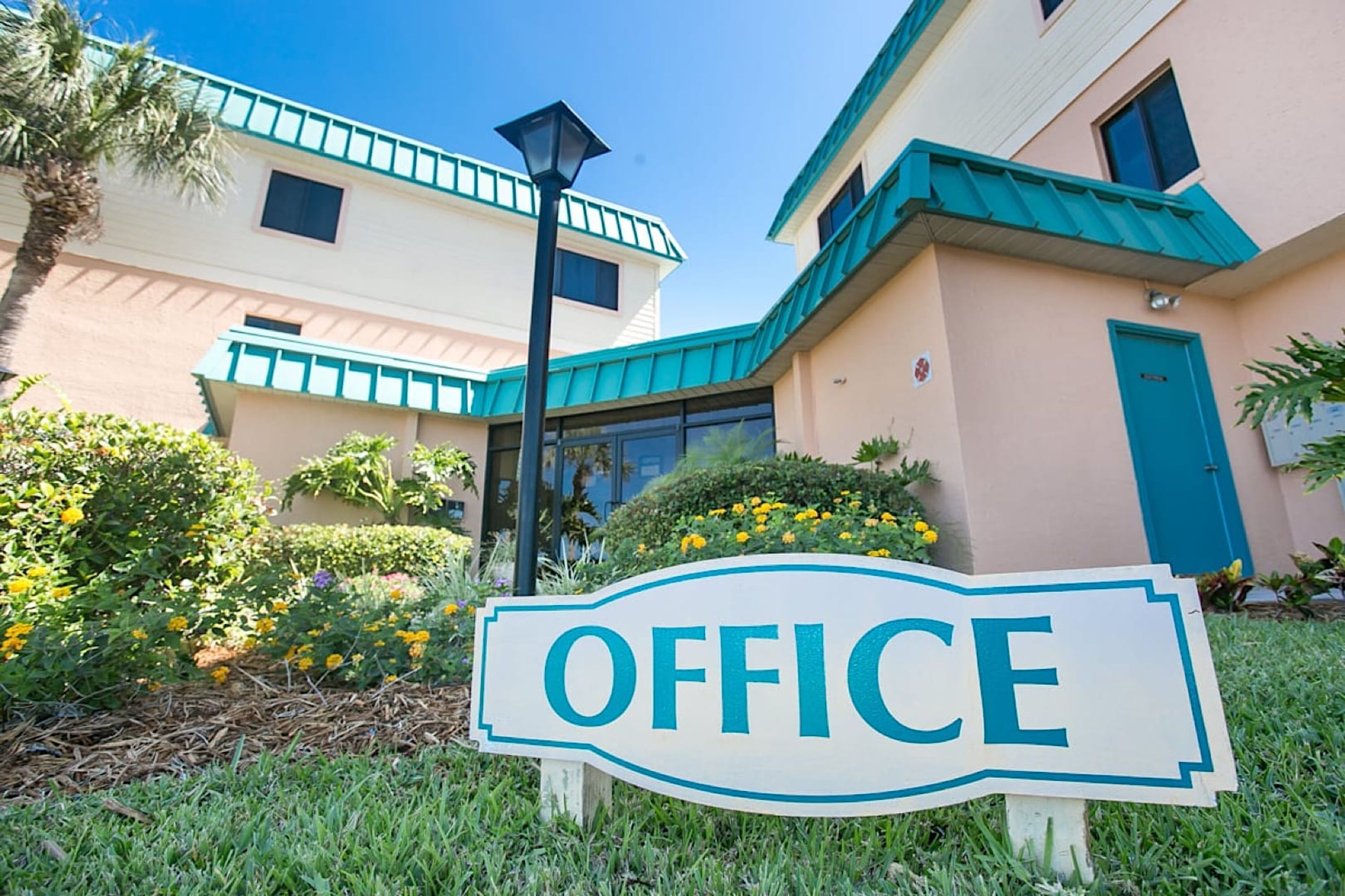 A building with a sign reading "OFFICE" in front, surrounded by greenery and a clear sky.