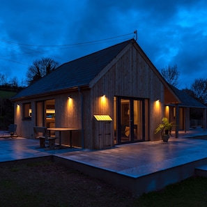 A wooden cabin with a sloped roof, large windows, and a patio area with seating. - Sunnybrook in Shaldon (Teignmouth)