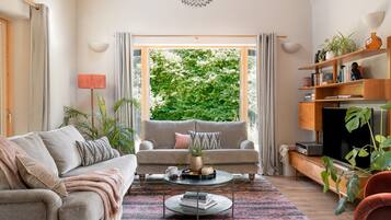 A living room with a sofa, coffee table, and a view of greenery outside.