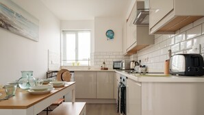A modern kitchen with white cabinets, a wooden countertop, and a dining area with a bench. - Quayside View in Paignton (Paignton)