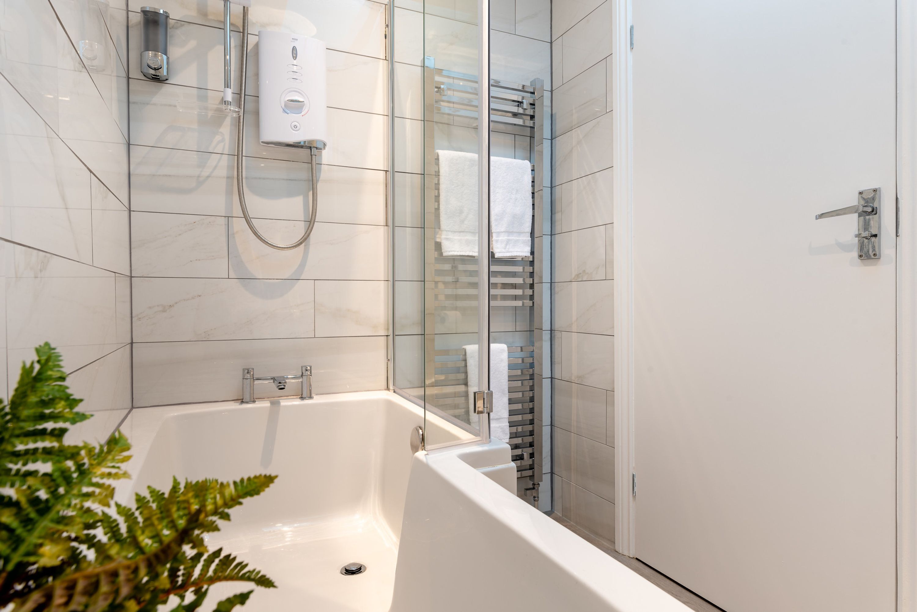 A modern bathroom with a glass-enclosed shower, a white bathtub, and a glass door.