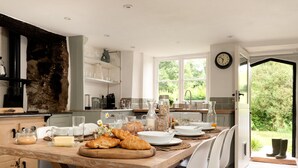 A modern kitchen with a wooden dining table set for breakfast, featuring croissants, bread, and a variety of breakfast items. - Weeke Brook in Chagford (Newton Abbot)