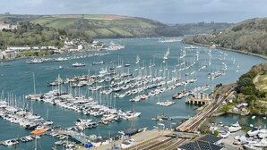 A marina with numerous boats docked, a train track running alongside, and a town in the background. - Two Guns in Kingswear (Dartmouth)