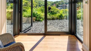 A room with a large sliding glass door leading to a gravel patio with a view of green hills and a clear sky. - Two Guns in Kingswear (Dartmouth)