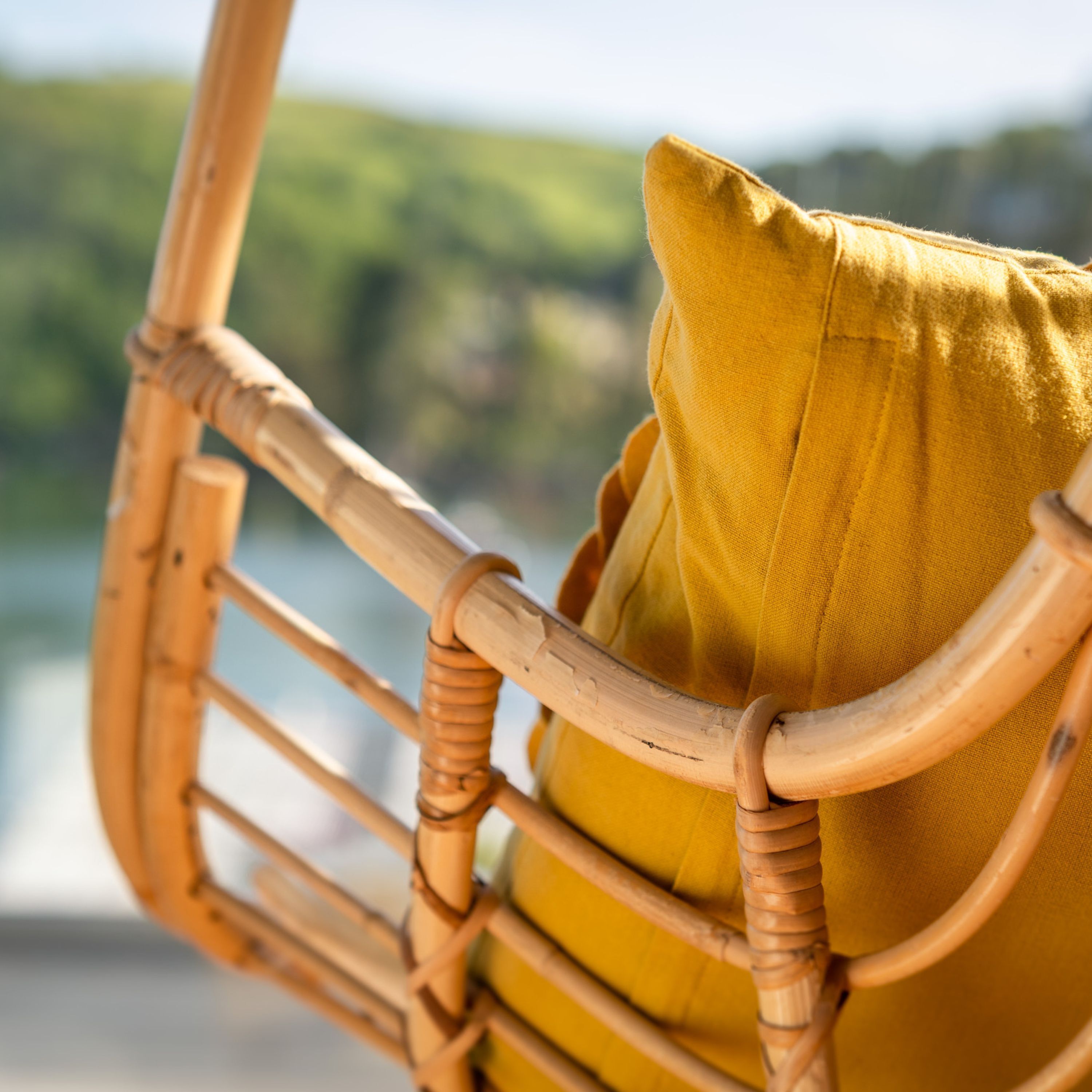Une chaise en osier avec un coussin jaune.