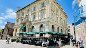 Un edificio histórico con entrada en esquina, mesas exteriores bajo sombrillas verdes y un letrero que dice “The Ivy”.