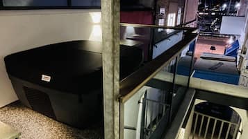 A balcony with a large black container, a metal railing, and a view of a street at night.