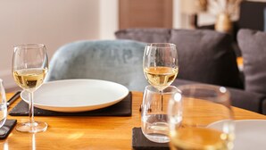 Een eettafel met twee wijnglazen en een bord, geplaatst in een woonkamer met een bank en een deur op de achtergrond.