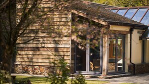 A wooden cabin with a stone foundation, large glass doors, and a covered porch. - Swallows End in Lower Ashton (Newton Abbot)