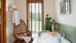 A bathroom with a bathtub, a wicker chair, a window with blinds, and a plant. - Higher Mapstone in Lustleigh (Newton Abbot)